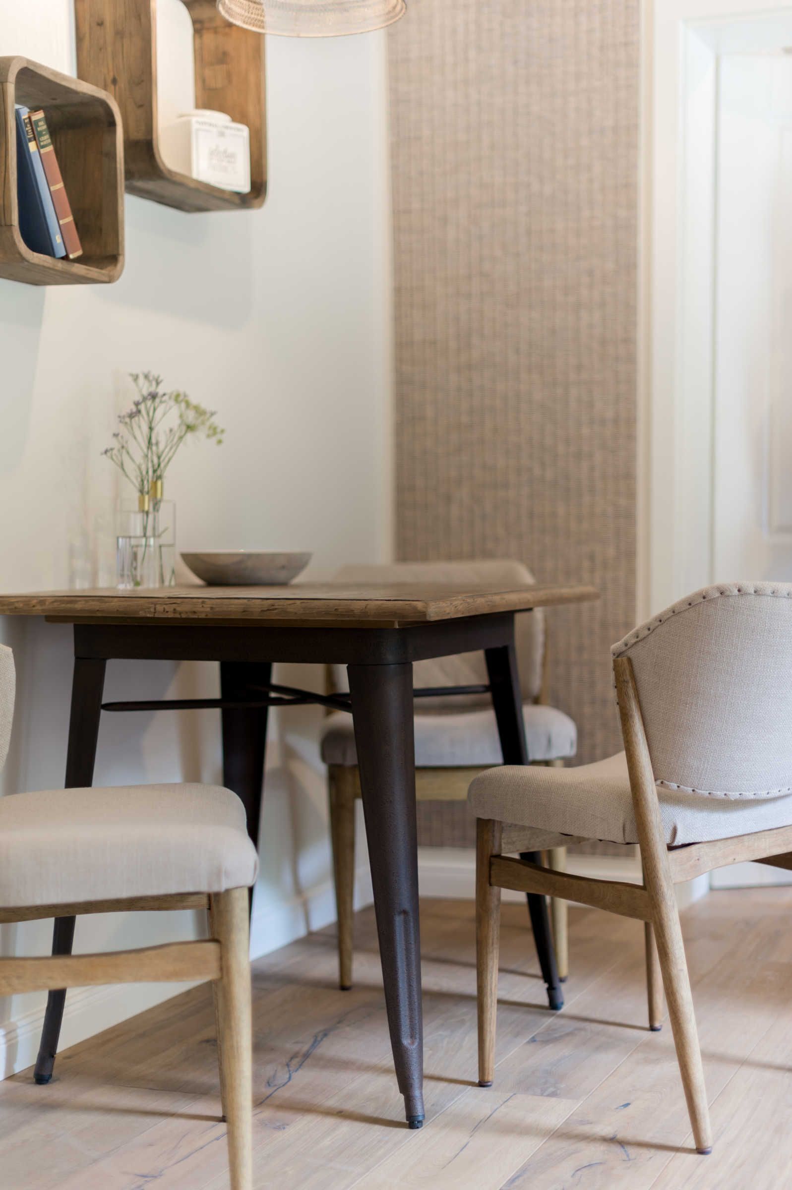 A dining area with a wooden table, two chairs, and a vase with flowers.