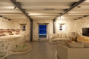 A room with stone walls, a sofa, a television, and a view of the outdoors. - Unique, luxurious villa with infinity pool and sea view, free WiFi (Kefalonia Fiskardo)