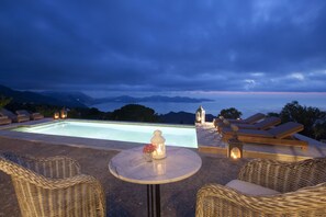A poolside area with wicker furniture, a table with a flower, and a view of the sea and mountains. - Unique, luxurious villa with infinity pool and sea view, free WiFi (Kefalonia Fiskardo)