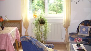 Una sala de estar con un sofá azul, una mesa de centro de vidrio y una mesa de comedor con mantel rosa.