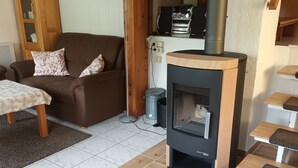 Una sala de estar acogedora con una estufa de leña, un sofá marrón con cojines estampados, un mueble de madera y una mesa con mantel decorado.