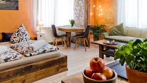 Una sala de estar acogedora con un sofá, una mesa de comedor con sillas, una mesita de centro de madera y un cuenco de fruta.