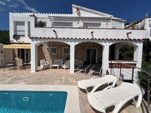 Un edificio de dos pisos con fachada de piedra, piscina y mobiliario exterior.