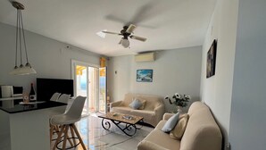 A modern living room with a sofa, a coffee table, a TV, and a ceiling fan. - CASA MIREILLA - Apartment with perfect sea view & private pool (El Mas Fumats)