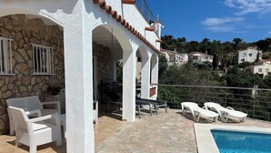 A villa with a stone exterior, a pool, white wicker furniture, and a view of the surrounding landscape. - CASA MIREILLA - Apartment with perfect sea view & private pool (El Mas Fumats)