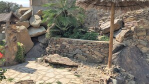 A stone pathway leading to a thatched-roof structure surrounded by rocks and greenery. - CASA MIREILLA - Apartment with perfect sea view & private pool (El Mas Fumats)