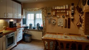 Una cocina con armarios de madera, una estufa, una mesa de comedor con sillas y diversos utensilios y electrodomésticos en las paredes.