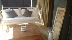 Una terraza de madera con un sofá blanco y cojines, una mesa de madera y una jarrón blanco.