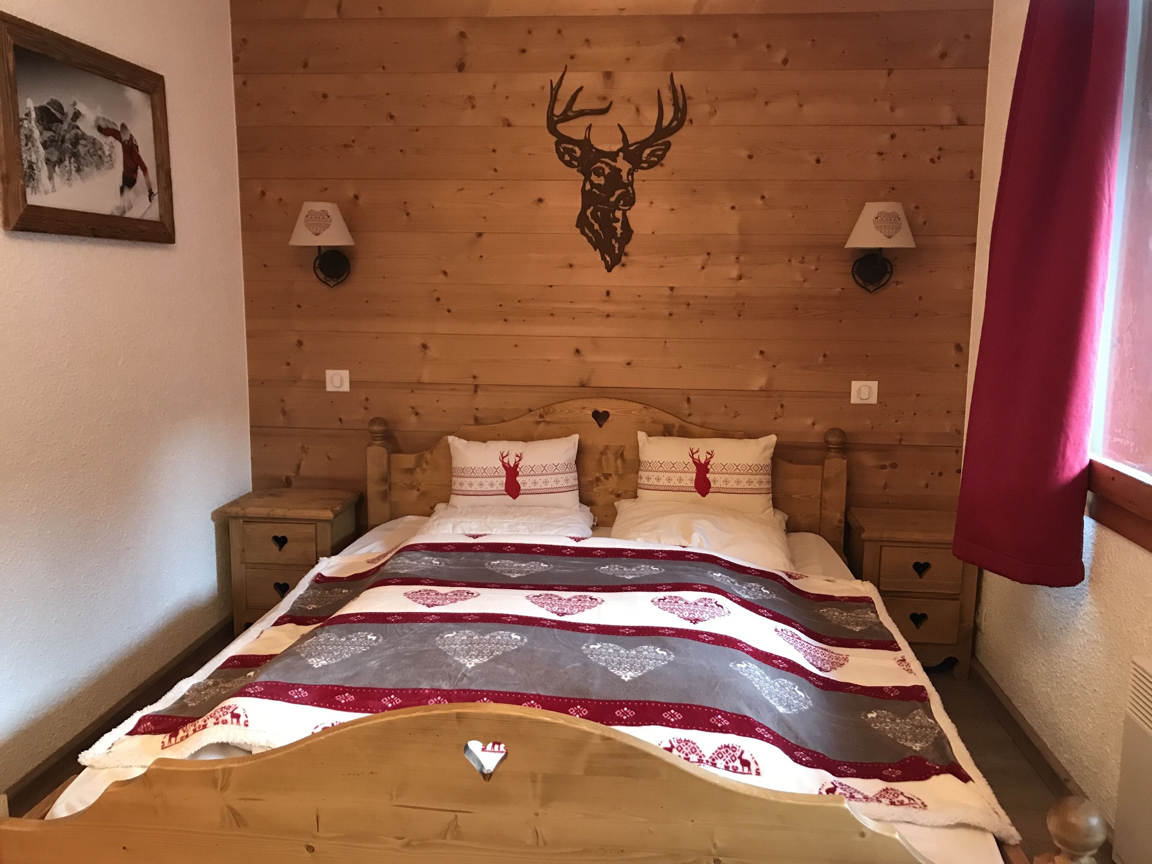A wooden-paneled room with a bed, two bedside lamps, and a deer head decoration on the wall.