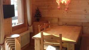 Un comedor de madera con una mesa, sillas, un pequeño árbol de Navidad y un televisor en la pared.