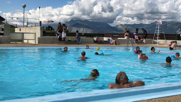 Una piscina con gente nadando, vistas de montañas y cielo despejado.