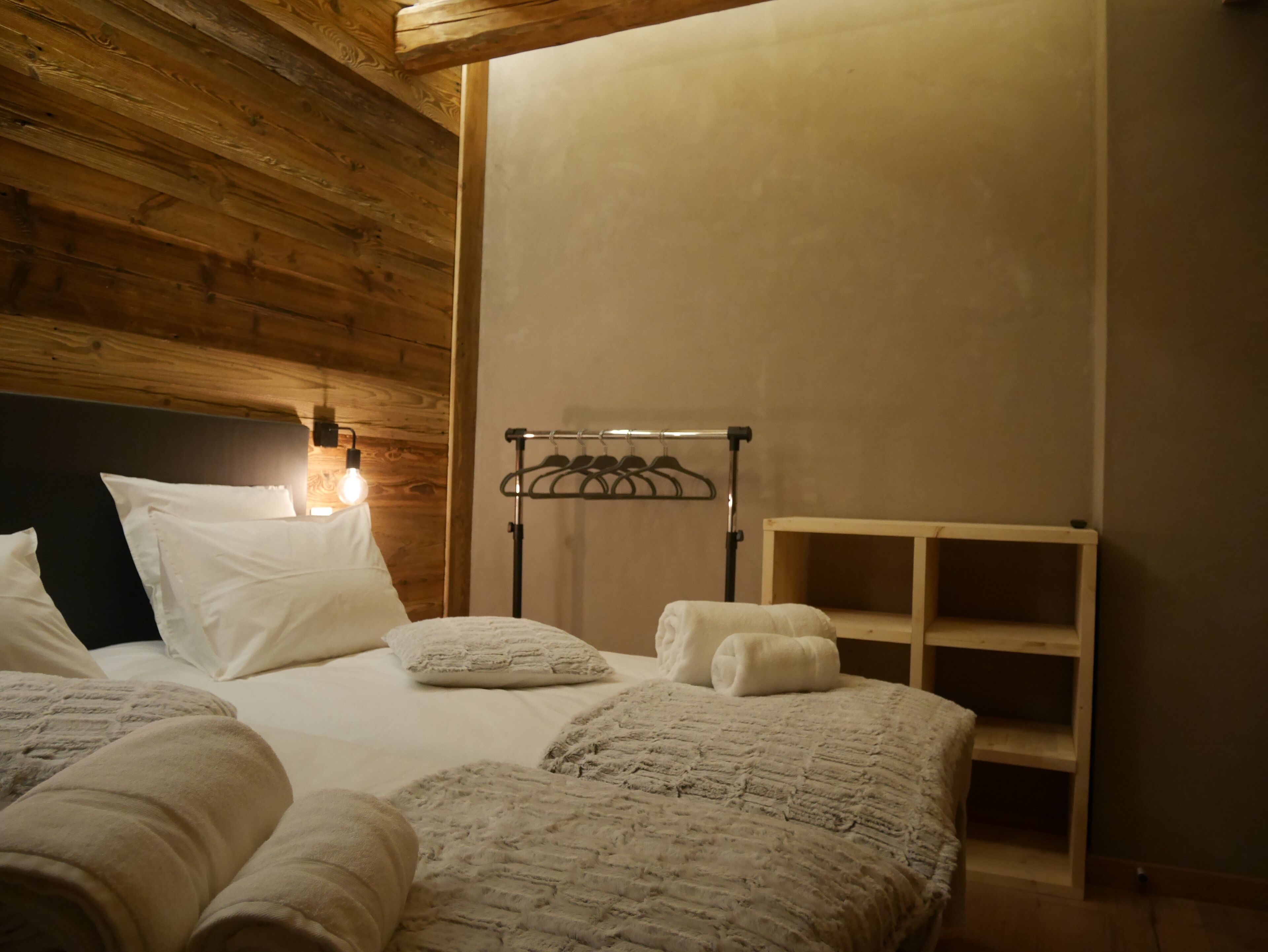 Un dormitorio con techo de madera, una cama con ropa de cama blanca, una mesita de noche y una lámpara de pared.