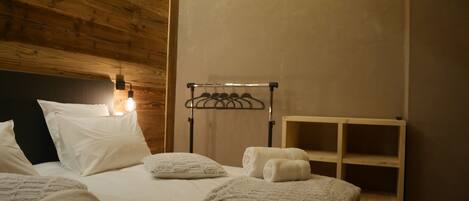 Un dormitorio con techo de madera, una cama con ropa de cama blanca, una mesita de noche y una lámpara de pared.
