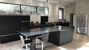 Una cocina moderna con una isla grande, armarios negros, electrodomésticos de acero inoxidable e iluminación colgante.