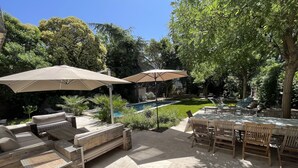 Un patio con mobiliario exterior, una piscina y abundante vegetación.
