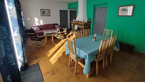 Ein Essbereich mit einem Tisch, gedeckt für vier Personen, umgeben von Holzstühlen. Im Wohnbereich befindet sich eine Couch und ein Couchtisch.