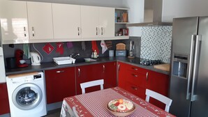 Eine kleine Küche mit einer Waschmaschine, einem Esstisch mit kariertem Tischläufer und einem Kühlschrank.