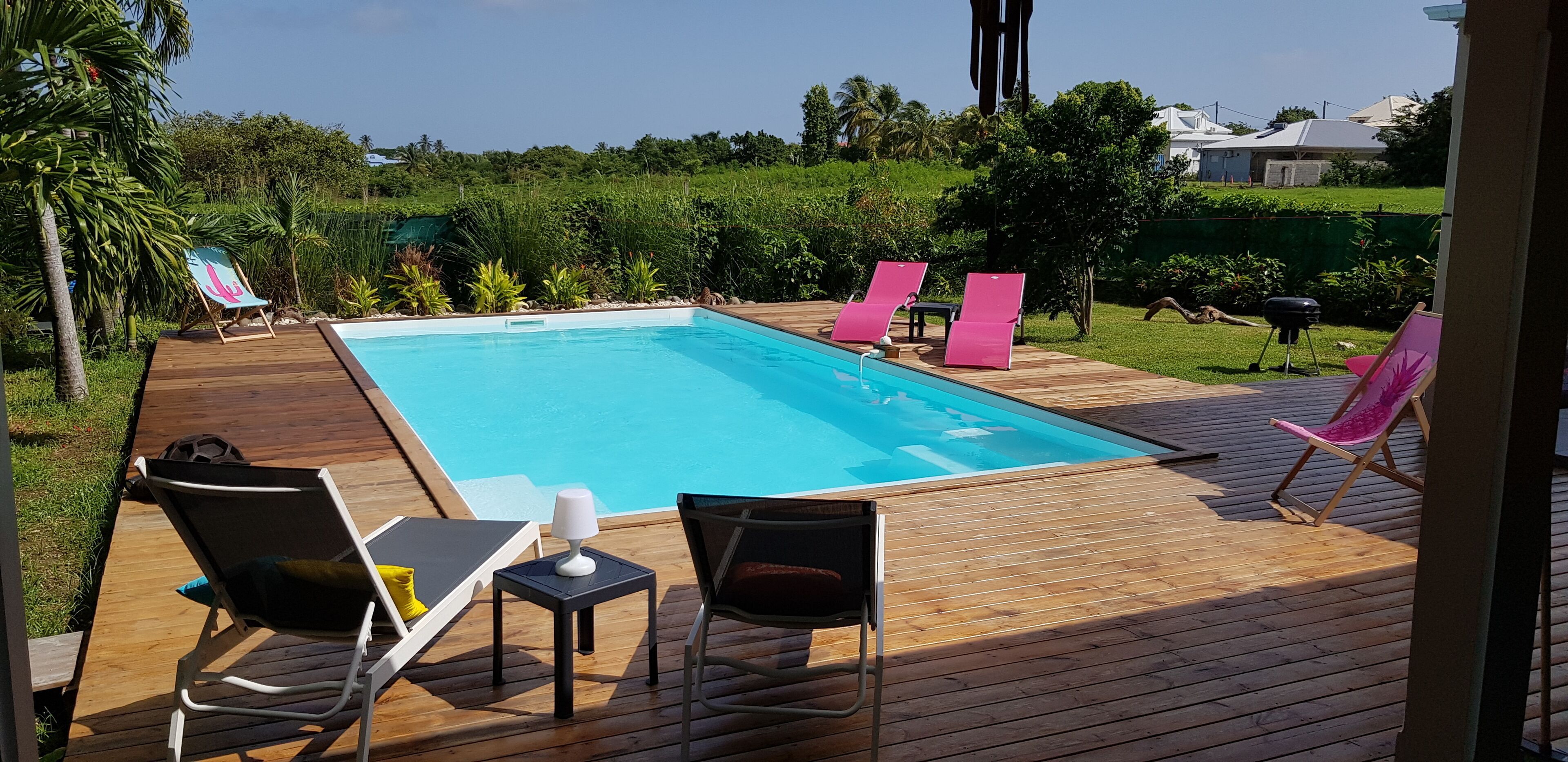 A wooden deck with a swimming pool, lounge chairs, and a table with a lamp.