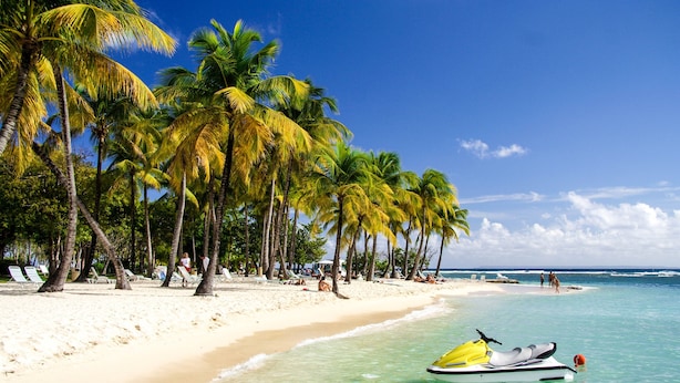 Une plage de sable blanc, des palmiers et un jet ski.