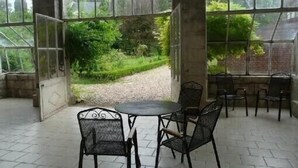 Ein überdachter Patio-Bereich mit Tisch und Stühlen, großen Fenstern und Blick auf einen Garten.