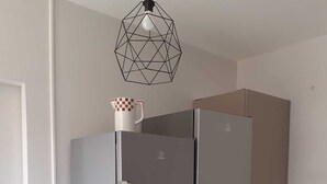 Eine moderne Küche mit einem Edelstahl-Kühlschrank, einer weißen Wand und einer geometrischen Pendelleuchte.