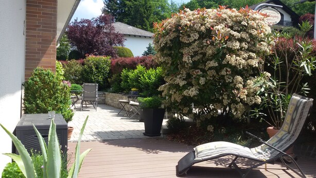 An outdoor patio with a chair, potted plants, and a large flowering bush. - Exclusive Holiday Apartment with Moselle View & Bike Garage (Bullay)