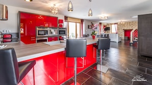 A modern kitchen with red cabinetry, stainless steel appliances, and a bar area with black stools. - 5-star villa with a pool available from August 29 to September 5 (Sainte Eulalie d'Olt)