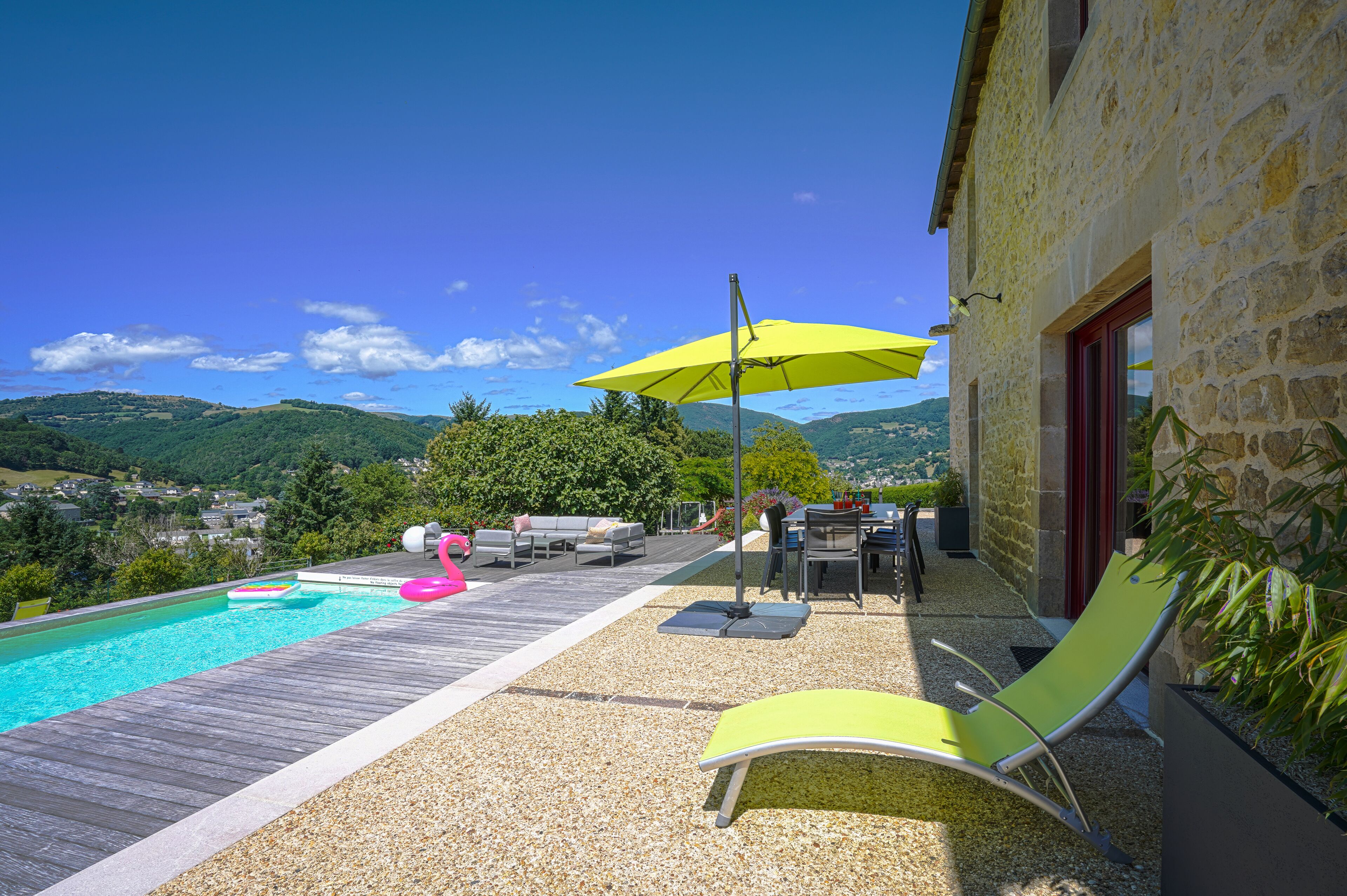 A poolside area with a wooden deck, a yellow umbrella, and a stone building.