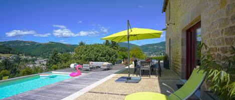 A poolside area with a wooden deck, a yellow umbrella, and a stone building.