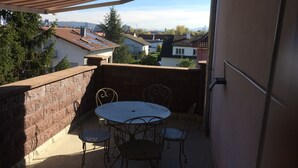 A balcony with a table and chairs, a striped awning, and a view of surrounding houses and trees. - Aviva (95 m2 apartment with terrace) (Huningue)