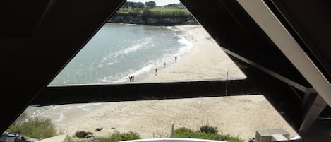 A beach view from a triangular window with a sandy shore and a calm sea.