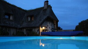Ein Haus mit einem Reetdach und einem Pool davor.