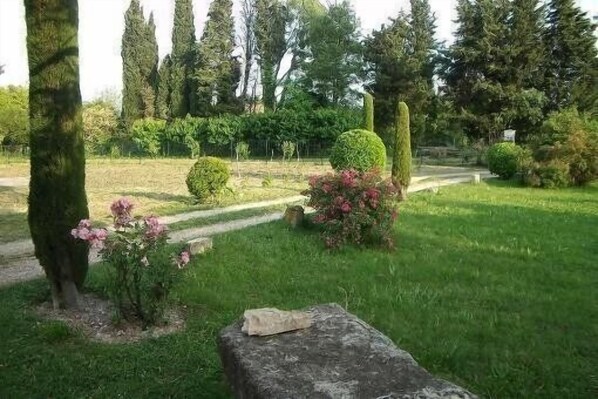 Un jardín con un banco de piedra, setos cuidadosamente recortados y árboles altos.