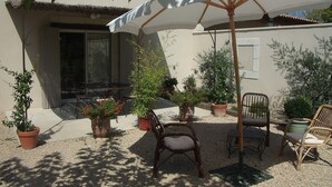Un patio al aire libre con una mesa y sillas, rodeado de plantas en macetas y un gran paraguas.