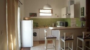 Cocina compacta con refrigerador, lavadora, microondas y un pequeño comedor con dos sillas.