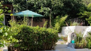 A garden area with a wooden bench, a green umbrella, and a stone wall with a water feature. - Villa in the countryside near Aix-en-Provence town center (Aix-en-Provence)