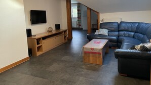 Un soggiorno con un divano in pelle blu scuro, un mobile porta TV in legno con diffusori, una TV a parete e un lucernario.