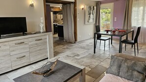 Un salon moderne avec un téléviseur, un coin repas avec une table et des chaises, et une cuisine en arrière-plan.