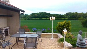 Une terrasse extérieure avec une table et des chaises, une statue et une vue sur un champ verdoyant.