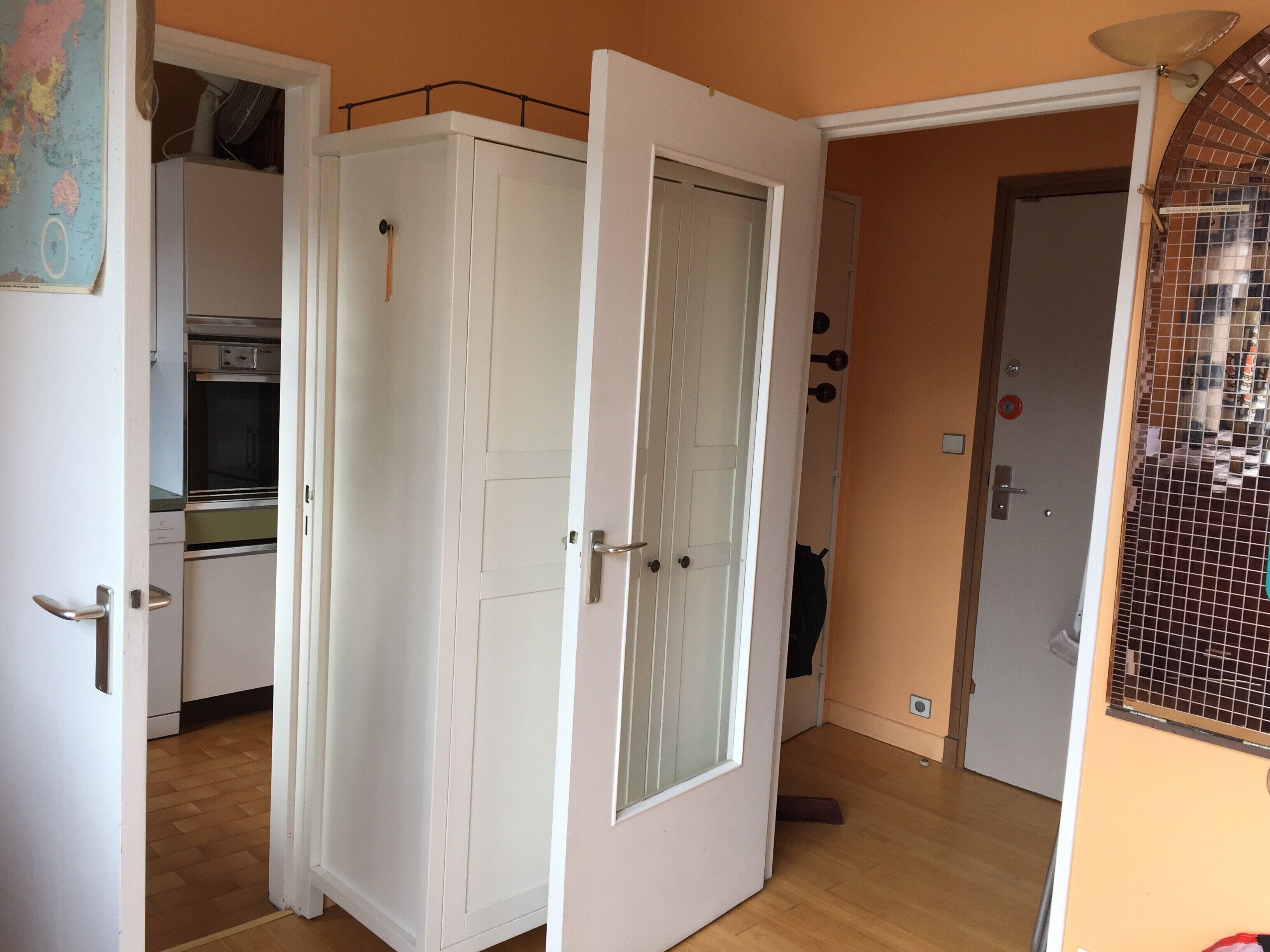 Una habitación con un armario blanco, una puerta con panel de cristal, un muro con azulejos y un suelo de madera.