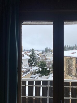 Une vue à travers une fenêtre à cadre en bois, donnant sur un quartier résidentiel enneigé avec des maisons et des arbres.