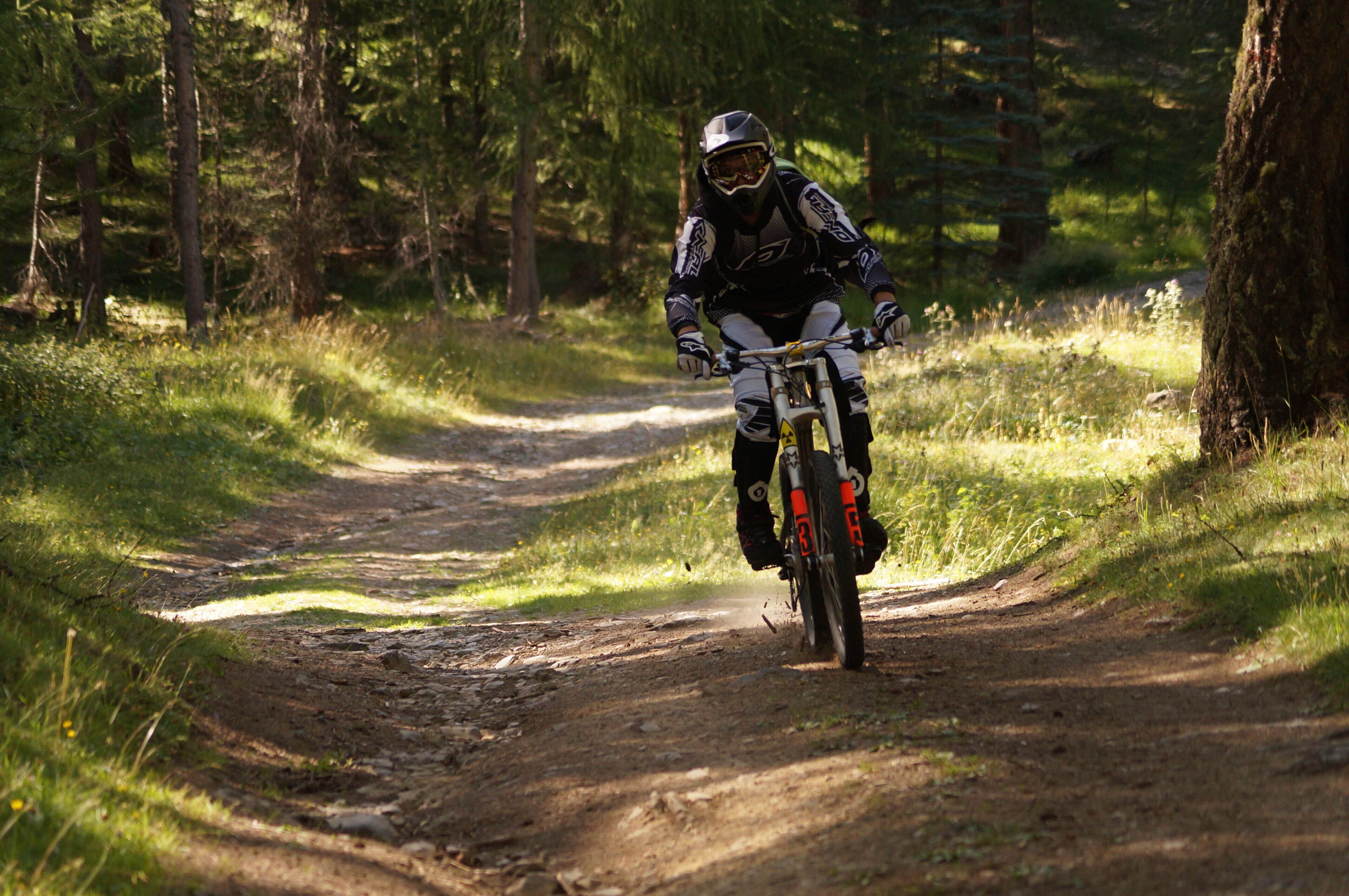 A person riding a motorcycle on a dirt path surrounded by trees.