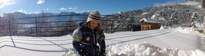 A person in winter clothing standing in a snowy landscape with mountains in the background and a wooden cabin. - T3 attic with private garden, air-conditioned Tennis court, EV terminal in a 2-hectare park. (EMBRUN)