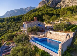 Une villa en pierre dotée d’une piscine, entourée d’une végétation luxuriante et de montagnes.