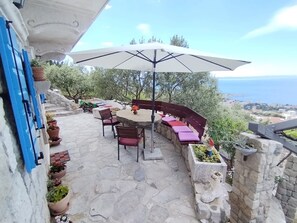 An outdoor patio with stone flooring, a round table, chairs, a bench, and an umbrella. - Villa Pina in Makarska, private pool (Makarska)