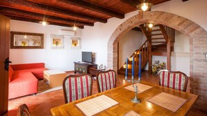 A cozy dining area with a wooden table, patterned chairs, and a brick archway leading to a staircase.