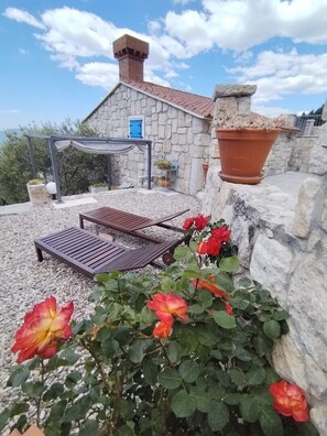 Un bâtiment en pierre avec un toit en tuiles, une pergola et un espace détente comprenant une table et des chaises.