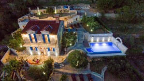 A large, multi-story building with a swimming pool, stone pathways, and outdoor seating areas.