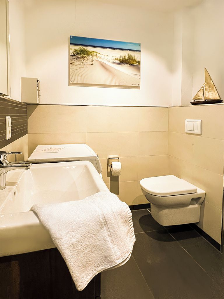 Une salle de bain moderne avec un lavabo, des toilettes et un tableau représentant une plage, accroché au mur.