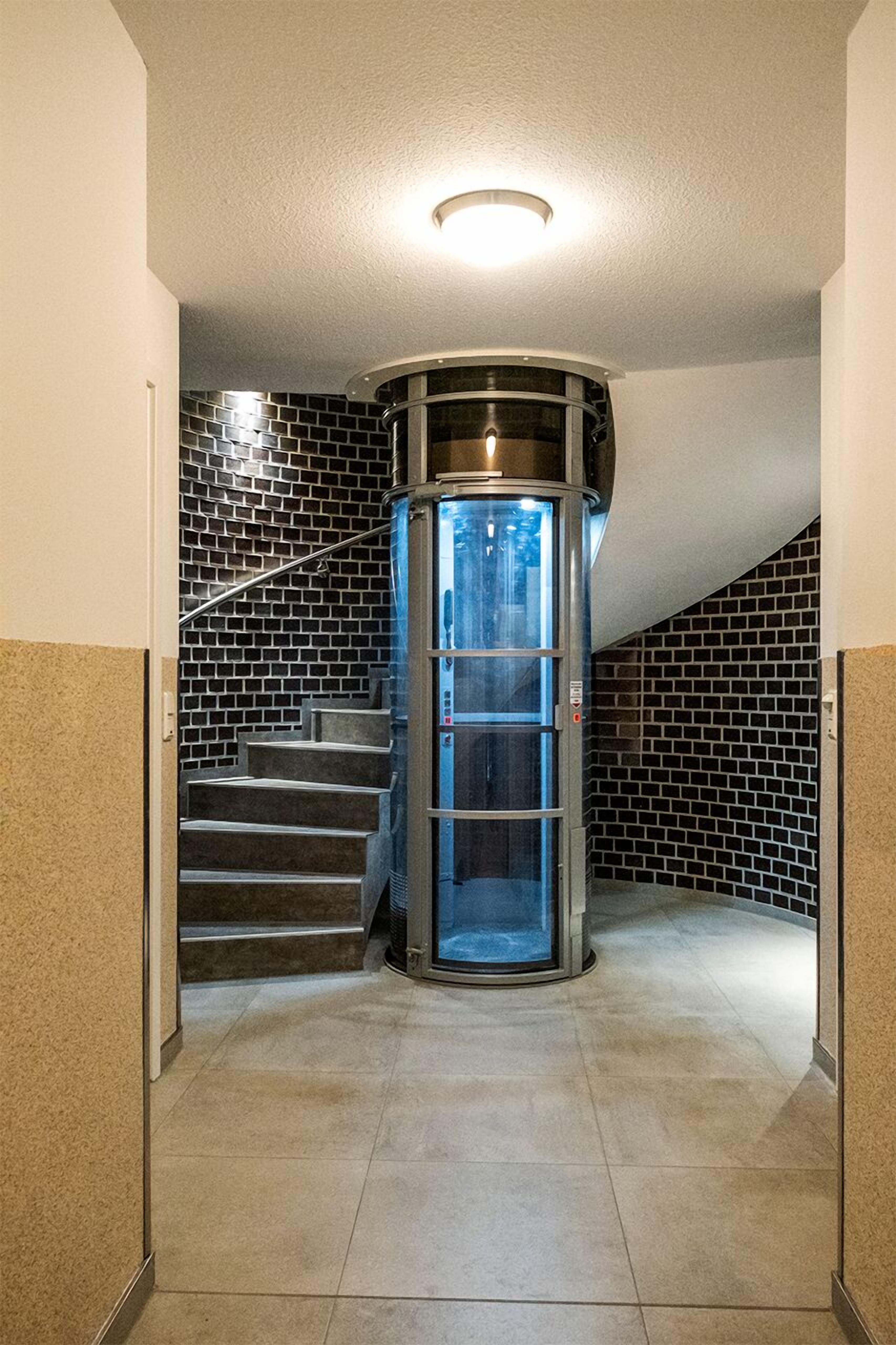 A modern elevator with a glass door, a staircase with black and white tiles, and a light fixture on the ceiling.